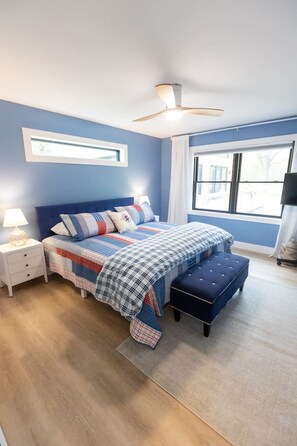 Un dormitorio con cama, mesitas de noche, ventilador de techo, ventana y vistas al exterior.