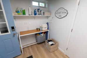Une buanderie équipée d’étagères, d’un panier et d’un panneau indiquant qu’il s’agit d’un service en libre-service, disponible 24 heures sur 24.