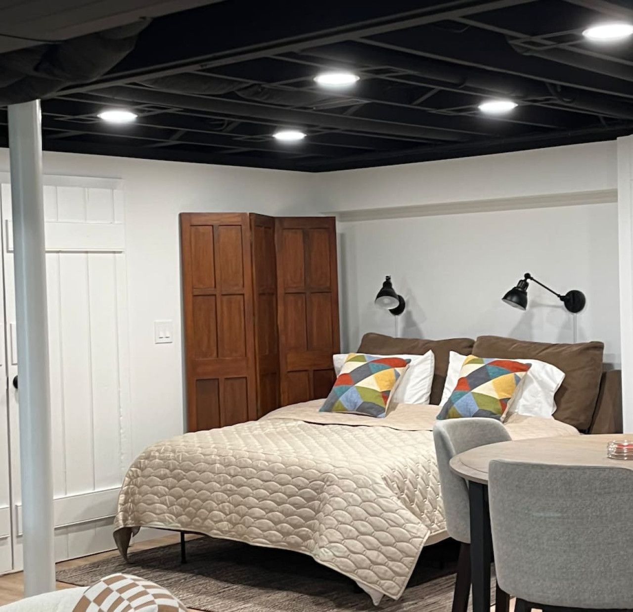 A bedroom with a bed, two bedside lamps, a wooden wardrobe, and a small table with chairs.