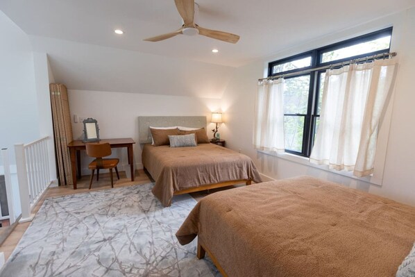 Une chambre avec deux lits, un bureau, une chaise, un ventilateur de plafond et une fenêtre avec des rideaux.