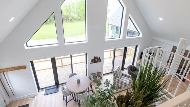 A spacious loft with high ceilings, large windows, and a view of a deck and greenery. - Camp Wagoner Lake Cabins (Mayfield)