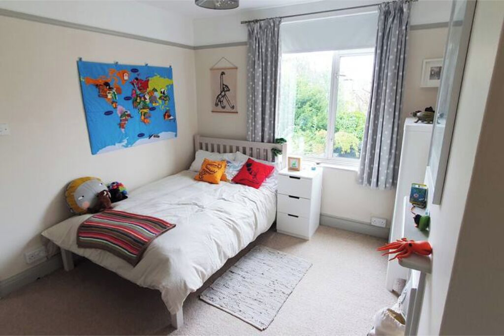 A bedroom with a bed, a nightstand, a window with curtains, a map on the wall, and a stuffed toy on the bed.