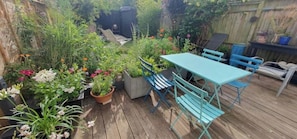 Una terraza de madera con una mesa y sillas, rodeada de plantas y flores en macetas.