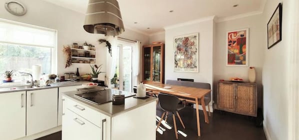 Una cocina moderna con armarios blancos, una isla central y un comedor con mesa y sillas de madera.