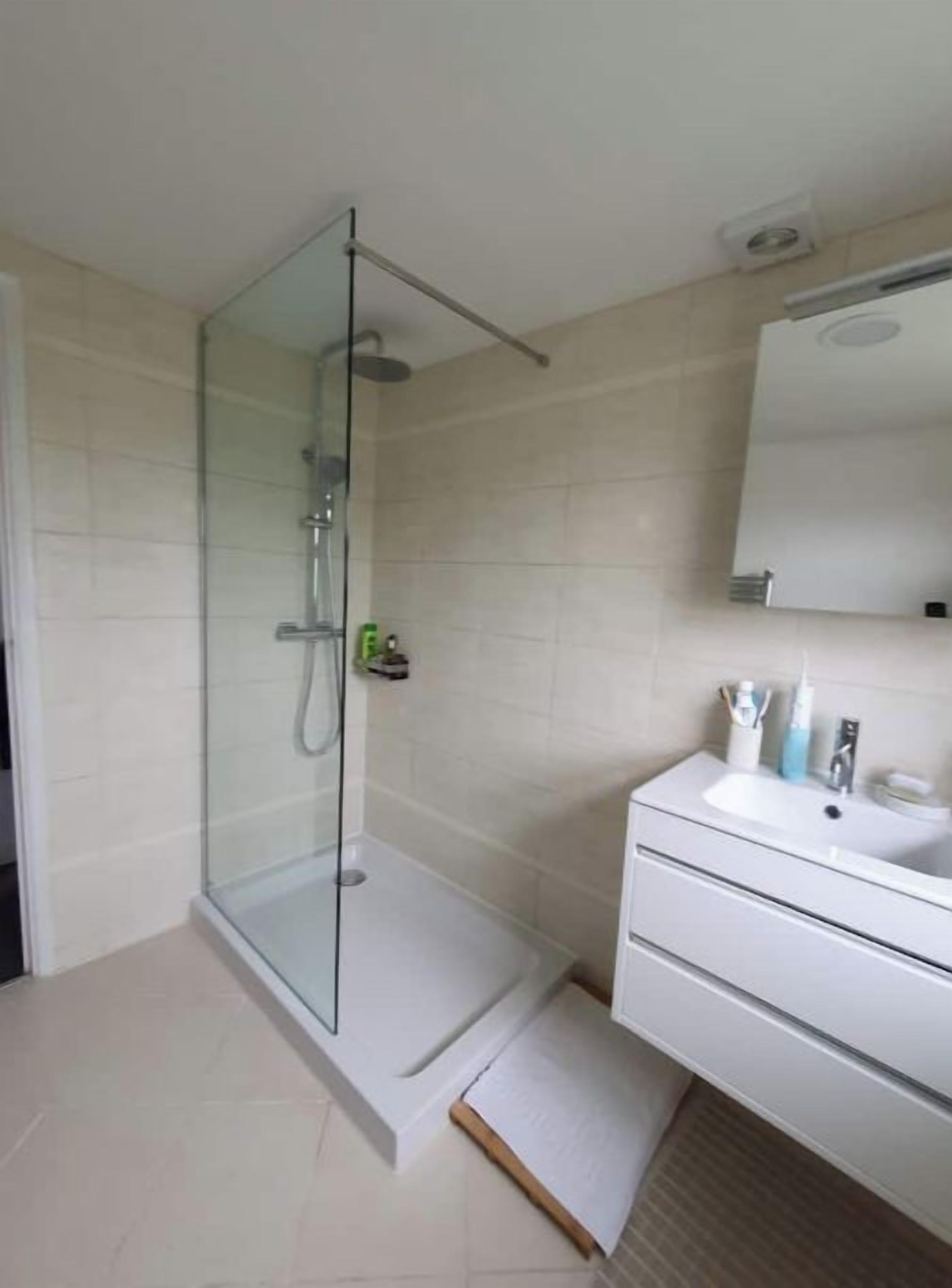Een moderne badkamer met een douchecabine van glas, een wit wastafelmeubel en een spiegel erboven.