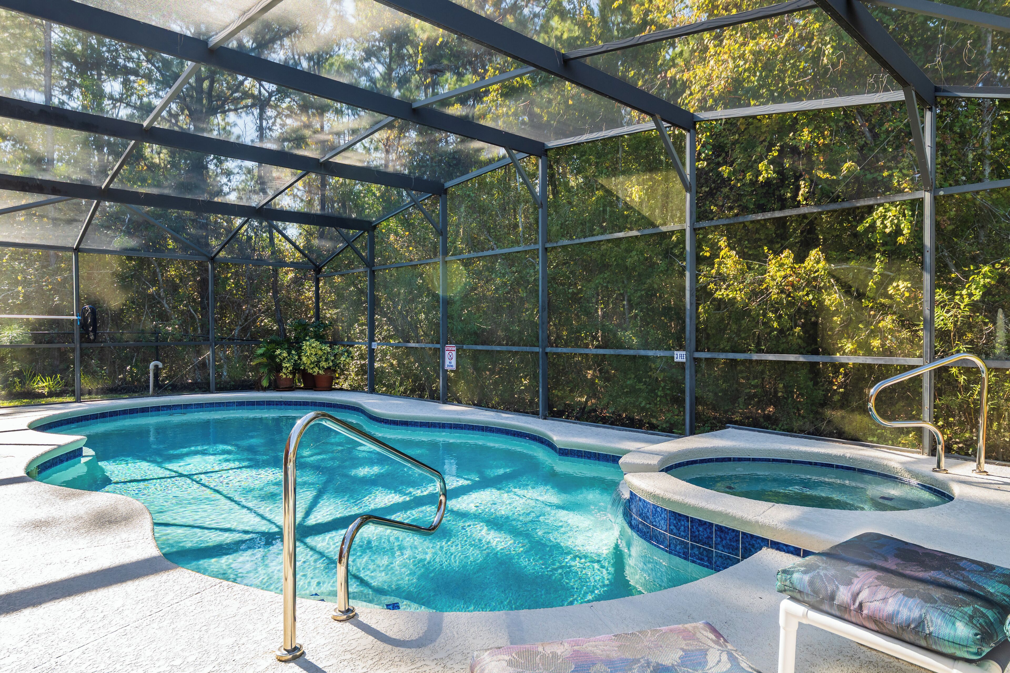 A swimming pool with a glass enclosure, a hot tub, and a lounge area with a cushion.