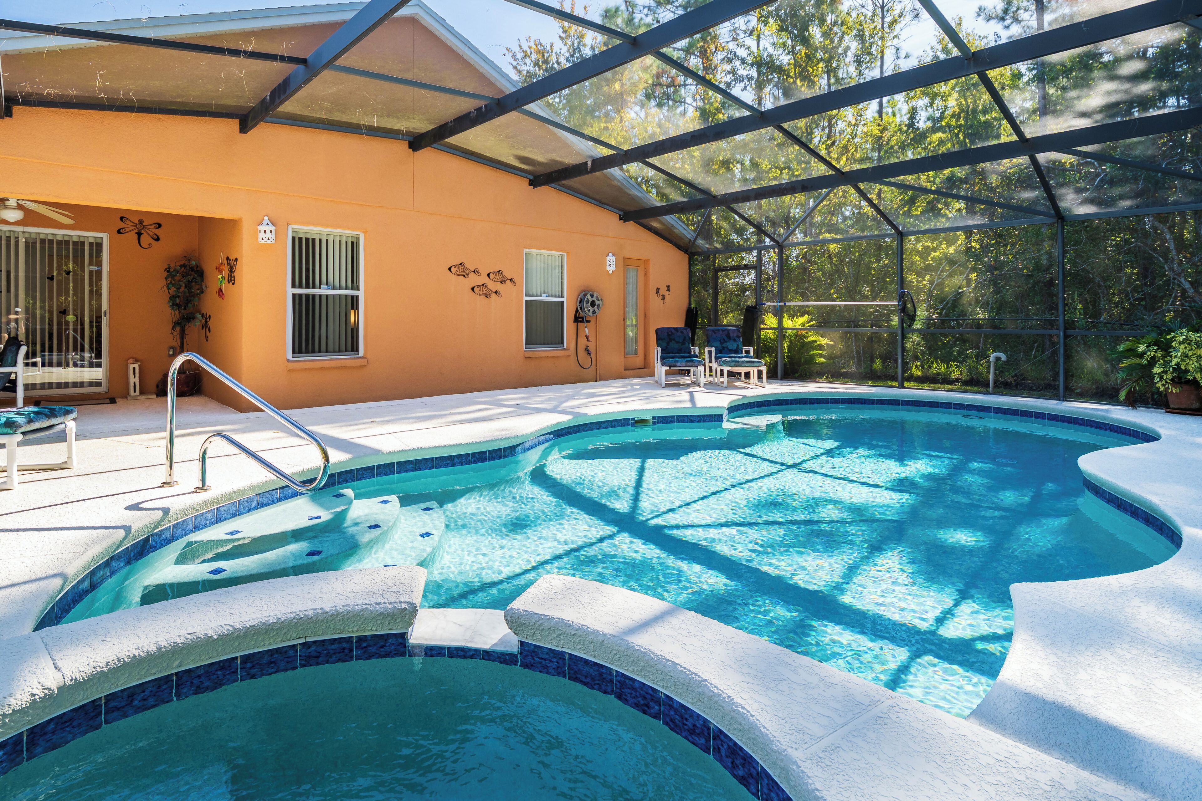 A swimming pool with a glass enclosure, a covered patio area, and a house with a peach exterior.