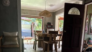 A dining area with a wooden table and chairs, a hanging light fixture, and a view of the outdoors through a glass door.