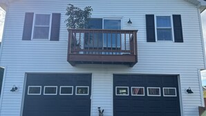 A two-story house with a balcony, two garage doors, and a small statue in front. - Private 2 bedroom lofted garage getaway. (Newport Center)