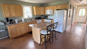 A spacious kitchen with wooden cabinets, a central island with stools, a refrigerator, and a microwave. - Private 2 bedroom lofted garage getaway. (Newport Center)