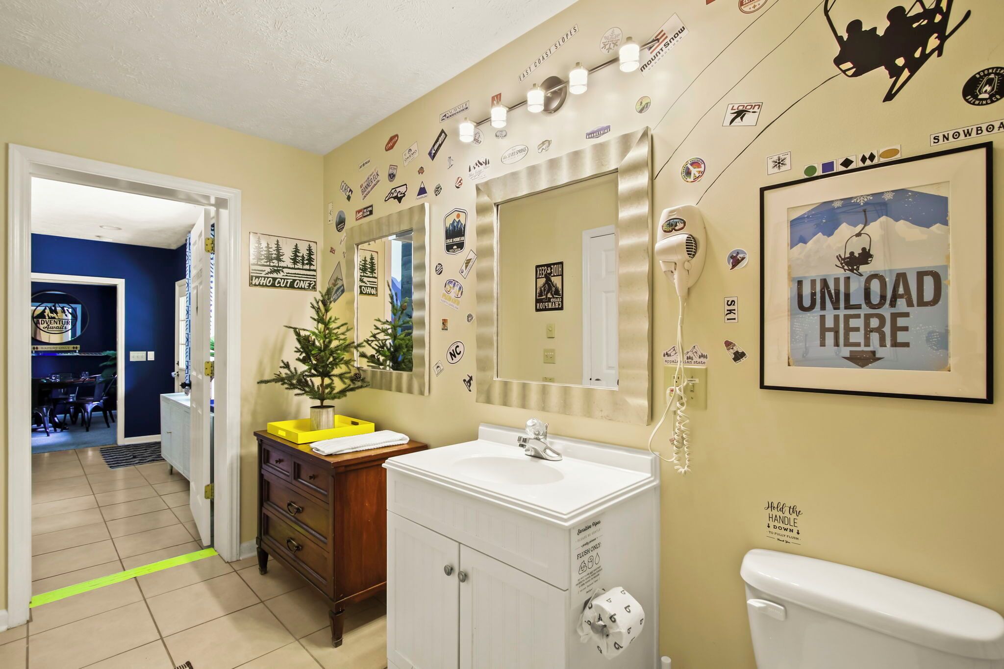 A bathroom with a sink, mirror, and toilet. There are stickers and a framed picture on the wall.