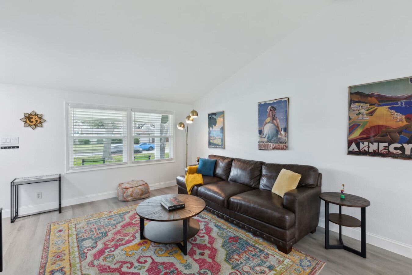 A living room with a brown leather sofa, a coffee table, a patterned rug, and a window with blinds.