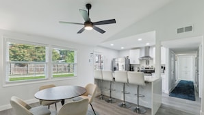 Une cuisine moderne avec des meubles blancs, un réfrigérateur en acier inoxydable et une cuisinière à gaz. On y trouve également un coin repas avec une table ronde et quatre chaises.
