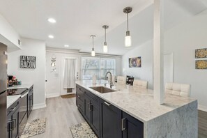 A modern kitchen with dark cabinets, a marble countertop, and pendant lighting. - Richardson Home Near SMU/ Dallas (Richardson)