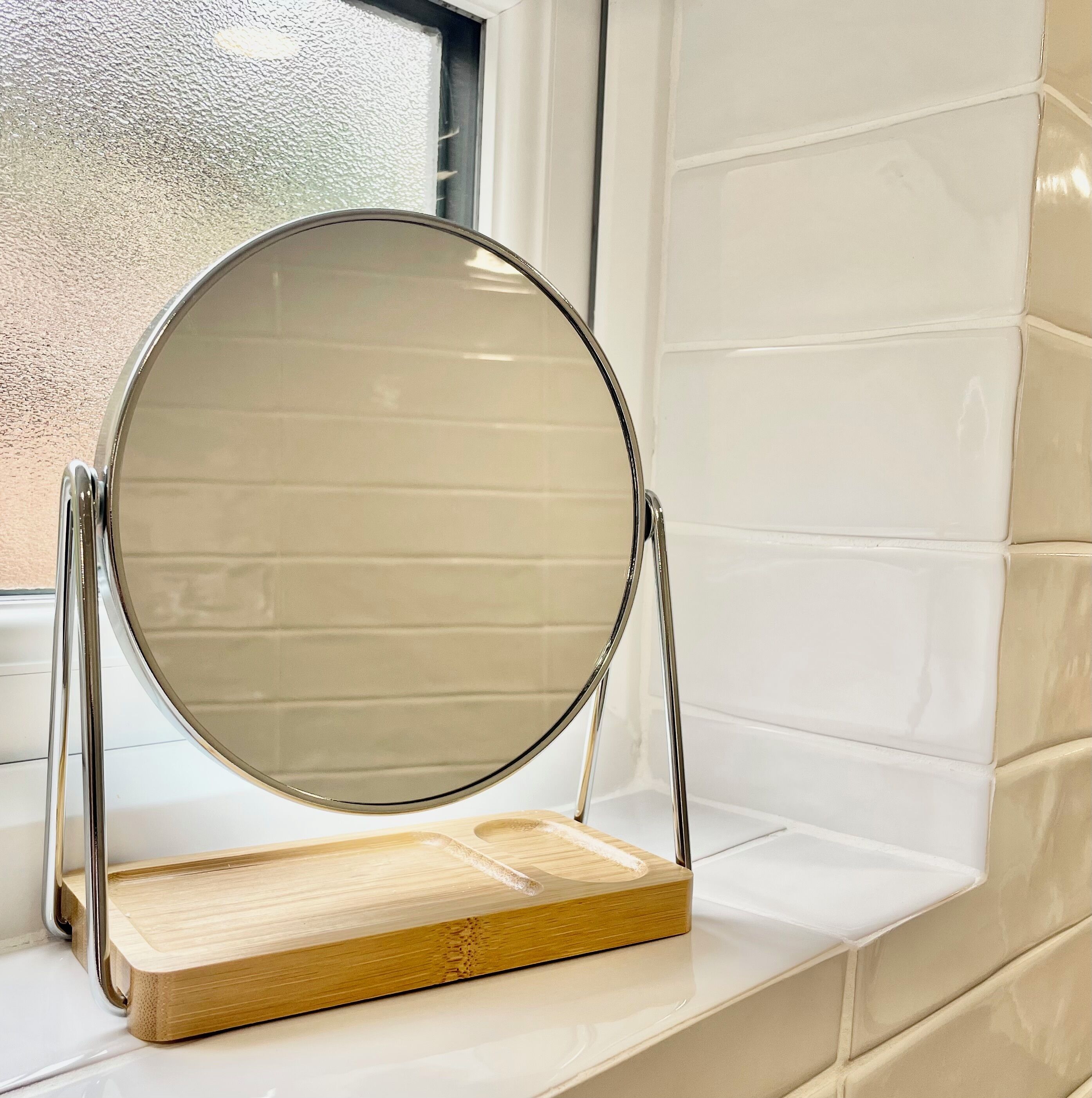 Een ronde spiegel met een houten voet op een witte betegelde rand.