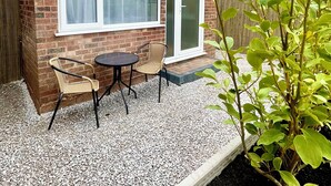 A small brick house with a patio, two wicker chairs, and a table. - The Cabin at No. 12 (Exeter)