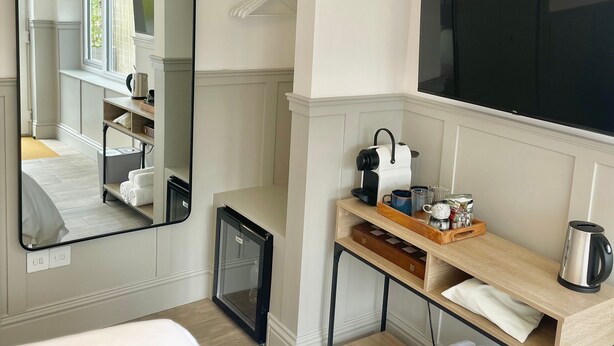 A hotel room with a bed, a mirror, a TV, a small kitchenette, and a window with a view of greenery. - The Cabin at No. 12 (Exeter)