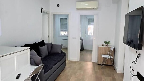 Una sala moderna con un sofá gris, una mesita blanca y un televisor montado en la pared.
