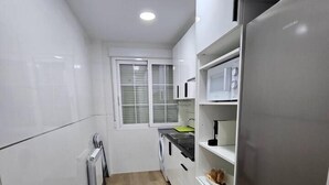 Una cocina moderna con armarios blancos, un refrigerador de acero inoxidable y una ventana con persianas.