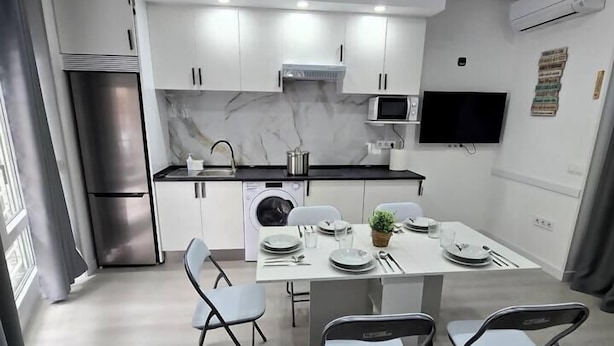 A modern kitchen with white cabinets, a stainless steel refrigerator, a microwave, and a dining table set for four. - Apartment in Southern Madrid for Groups/Families (Leganes)