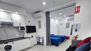 A hotel room with a kitchen area, a washing machine, a TV, and a bed with multiple pillows. - Apartment in Southern Madrid for Groups/Families (Leganes)