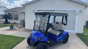 Un carrito de golf azul estacionado frente a un garaje blanco.