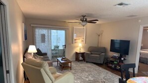 Una sala de estar con sofá, sillón, mesa de centro, televisor y ventilador de techo.