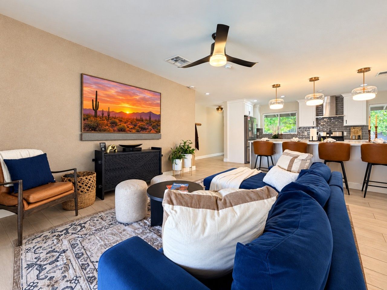 A living room with a sofa, chairs, a coffee table, and a painting of a desert sunset.