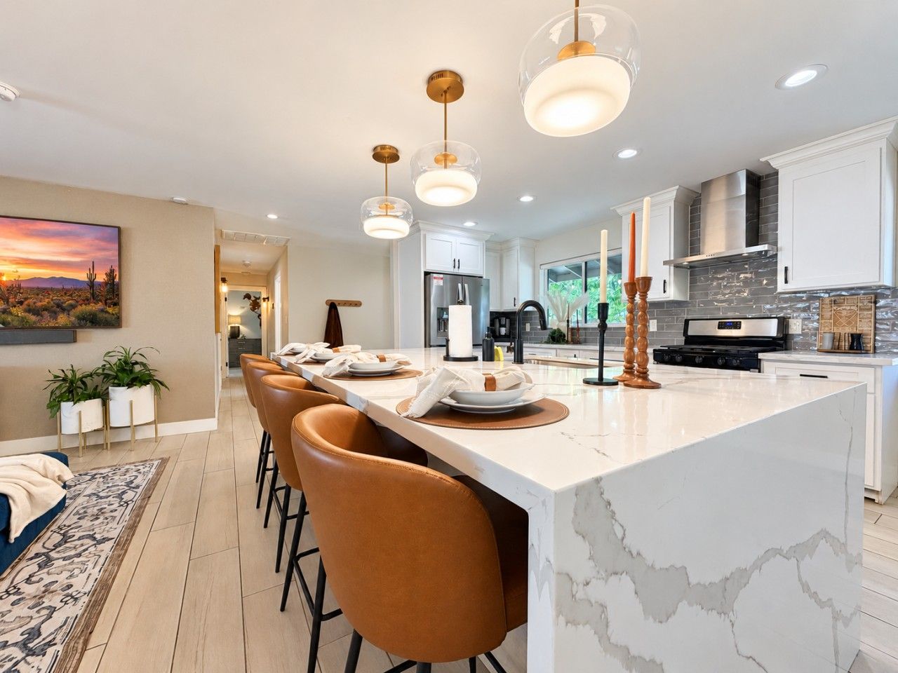 A modern kitchen with a marble island, pendant lighting, and a dining area with leather chairs.