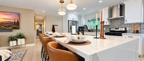 A modern kitchen with a marble island, pendant lighting, and a dining area with leather chairs.