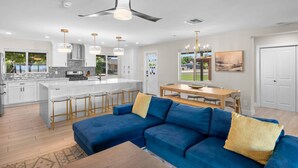 A modern kitchen with a central island, bar stools, and a dining area with a wooden table and chairs.