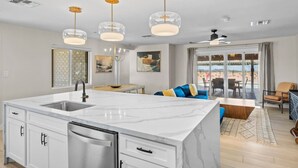 A modern kitchen with a central island, a dining area with a table and chairs, a living room with a sofa and a TV, and a balcony with a view.