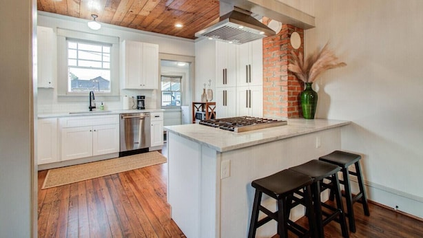 Una cocina moderna con gabinetes blancos, una pared de ladrillo decorativa y una isla central con taburetes.