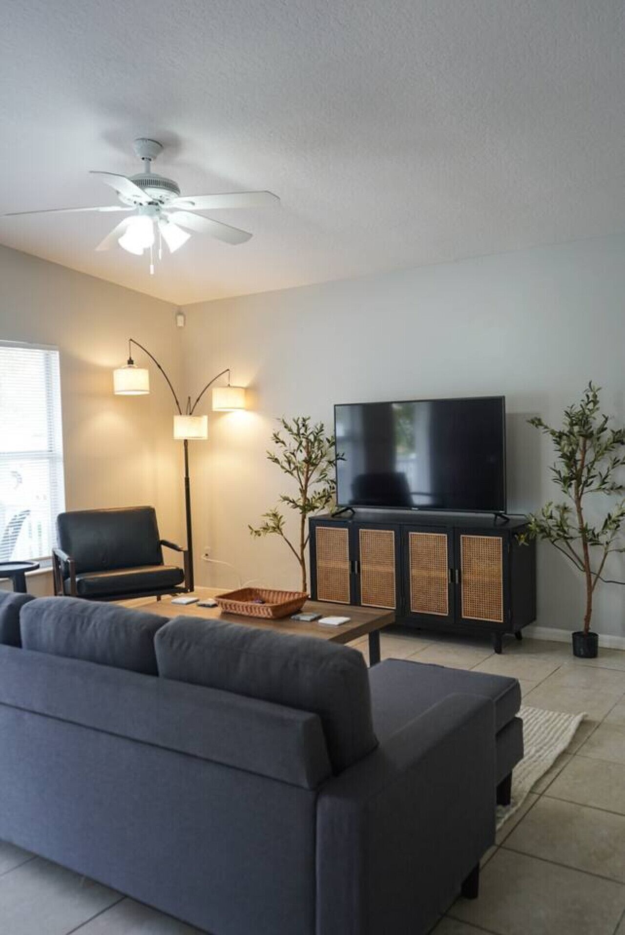 A living room with a sofa, a television, a ceiling fan, and two floor lamps.