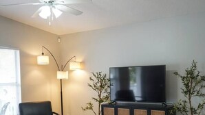 Un salon comprenant un canapé, un téléviseur, un ventilateur de plafond et deux lampadaires.