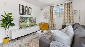A modern living room with a flat-screen TV, a yellow armchair, a grey sofa, and a potted plant.