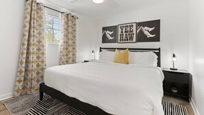 A modern bedroom with a large bed, a ceiling fan, and artwork on the wall.