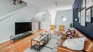 A modern living room with a flat-screen TV, a glass coffee table, and a leather sofa.