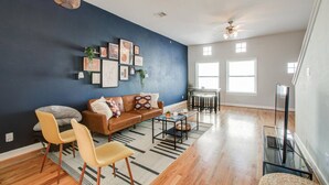 A spacious living room with a dark blue accent wall, a brown leather sofa, yellow chairs, and a glass coffee table.