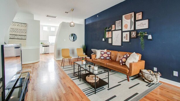 A modern living room with a dark blue accent wall, a leather sofa, and a glass coffee table.