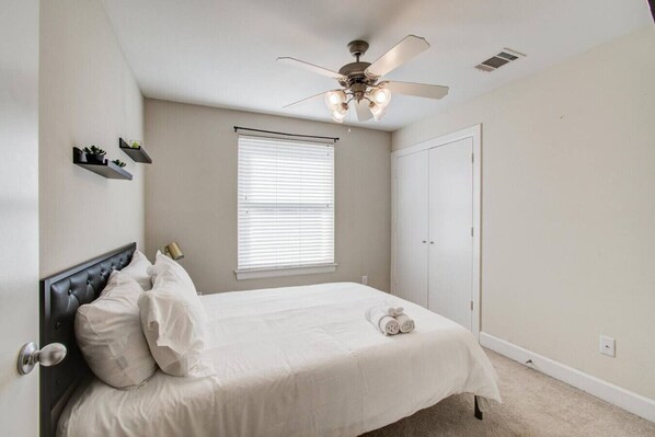 A bedroom with a bed, a ceiling fan, a window with blinds, and a door.