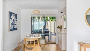 A modern dining area with a glass door leading to a staircase, wooden furniture, and a view of greenery outside.
