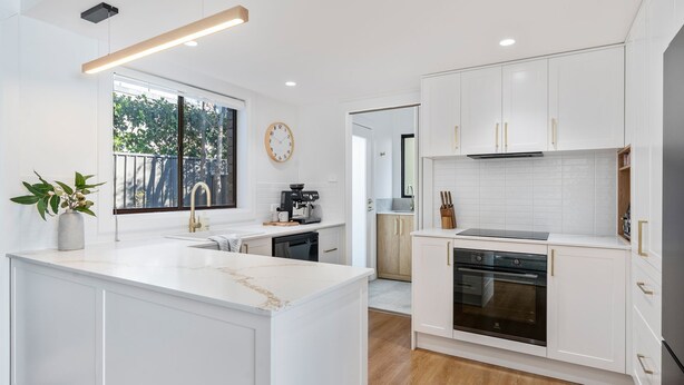 A modern kitchen with white cabinetry, a central island, a coffee machine, and a view of the outdoors through a window.
