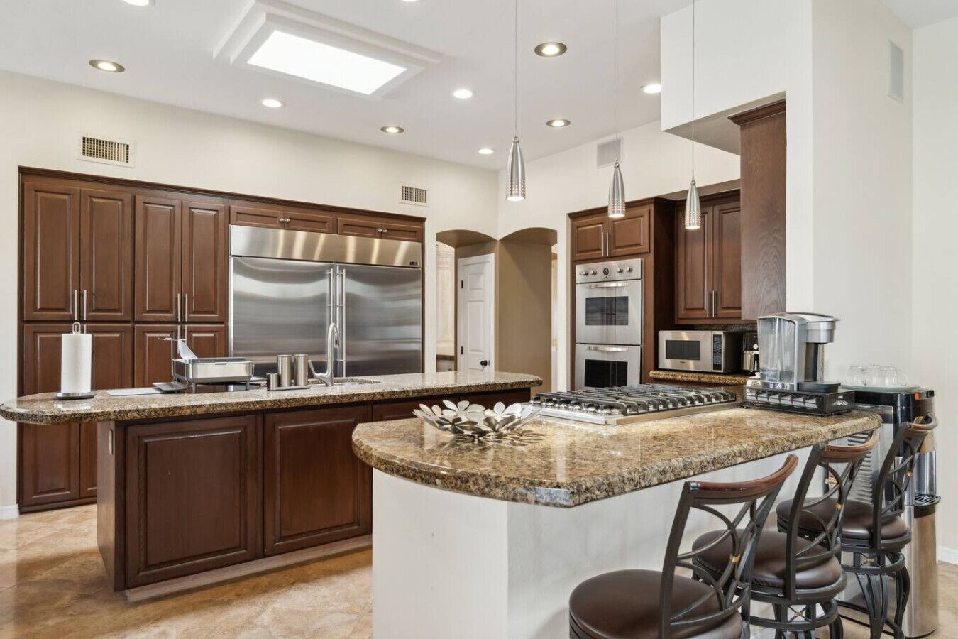 A modern kitchen with dark wood cabinets, stainless steel appliances, granite countertops, and bar stools.