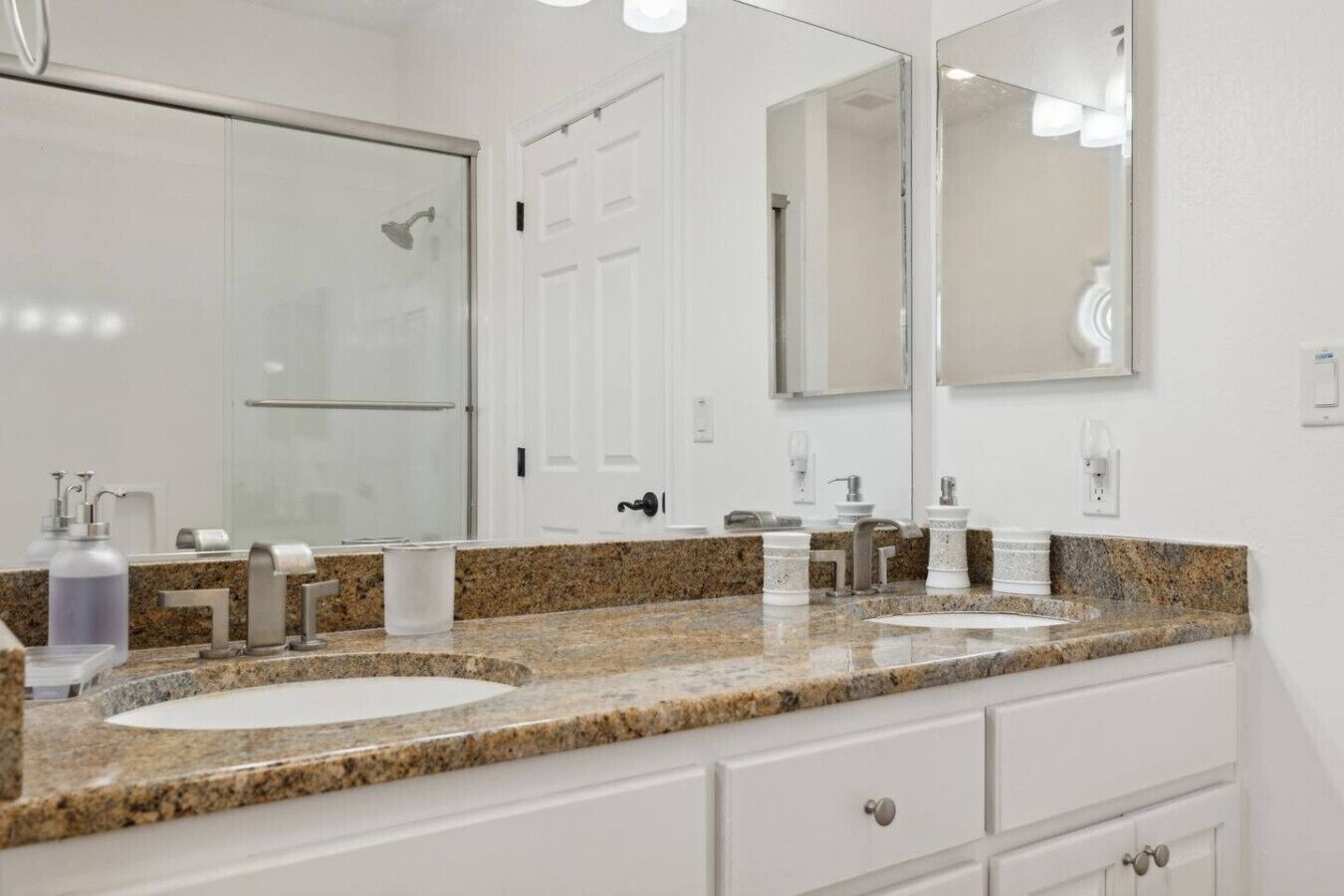 A modern bathroom with two sinks, a large mirror, and a shower.