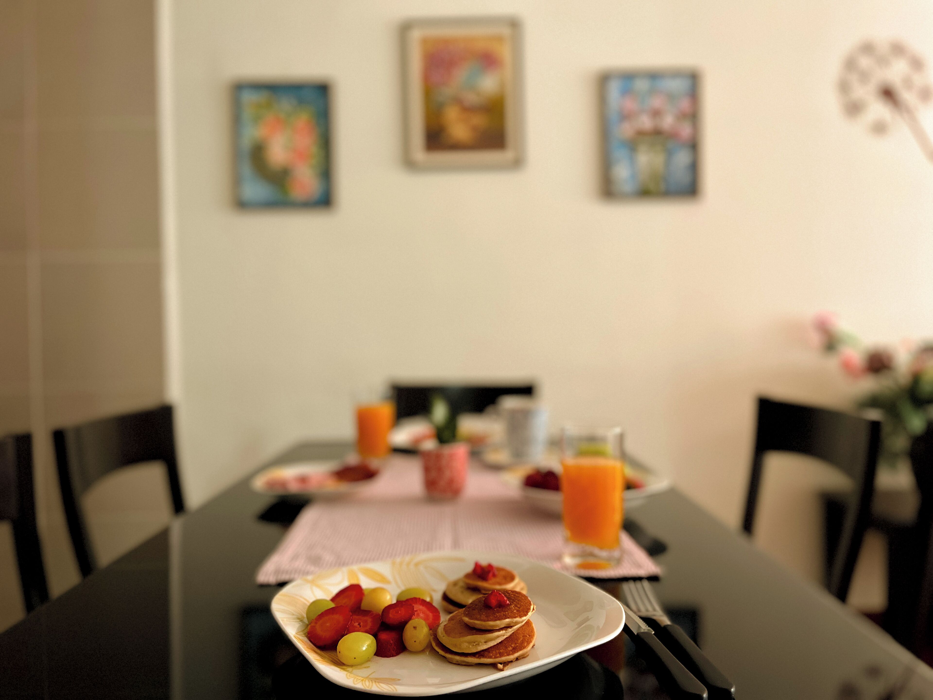 A breakfast table with pancakes, fruit, and orange juice.