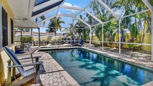 A covered swimming pool with lounge chairs and umbrellas, surrounded by palm trees and a clear sky. - Tropical Escape | Pool | Game Room | Near Beach (St. Petersburg)