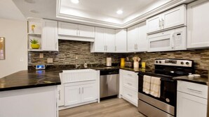 A modern kitchen with white cabinets, a black countertop, a stainless steel oven, and a microwave. - Tropical Escape | Pool | Game Room | Near Beach (St. Petersburg)