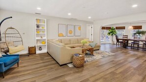 A spacious living room with a sofa, a hanging chair, a dining area with a table and chairs, and a large window providing natural light. - Tropical Escape | Pool | Game Room | Near Beach (St. Petersburg)
