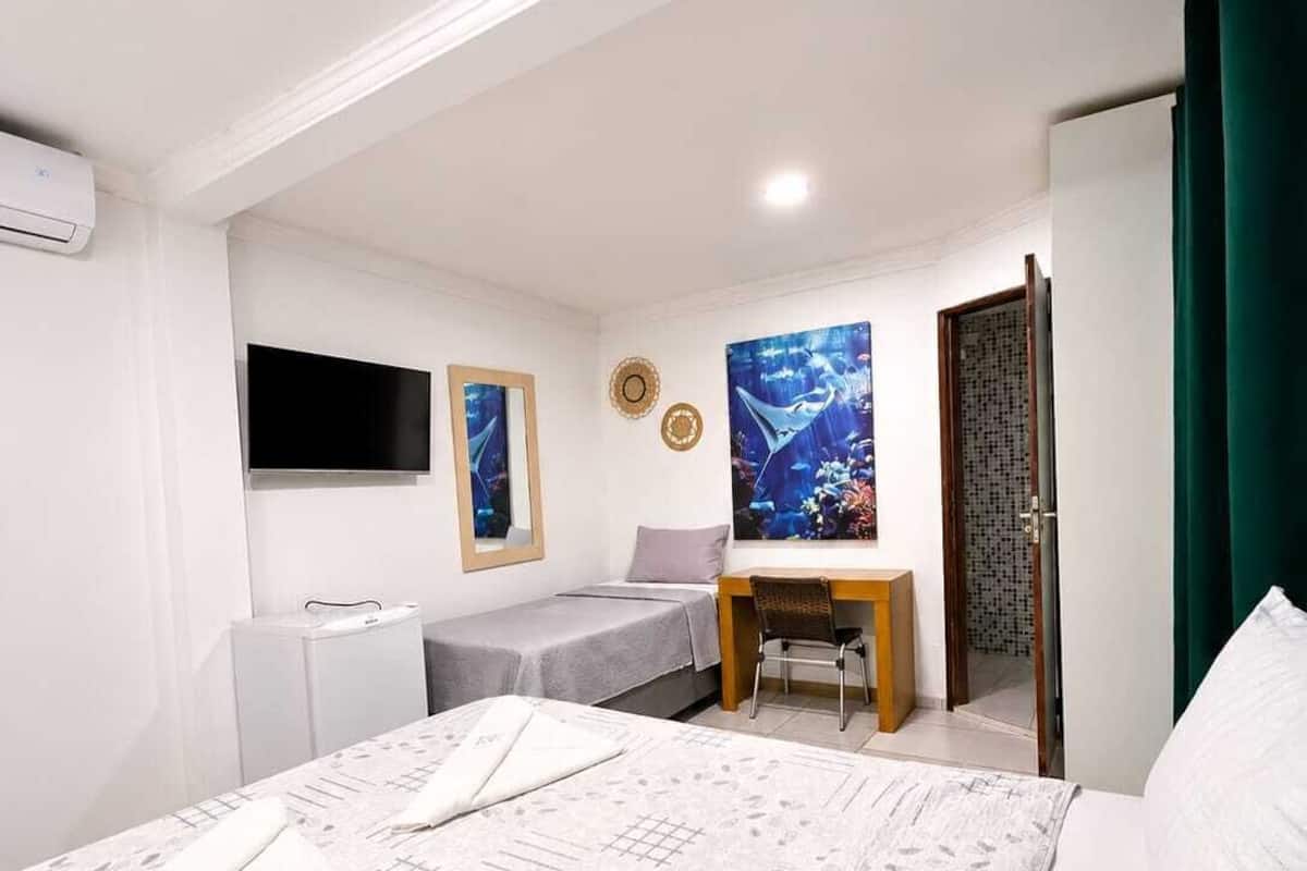 A bedroom with a bed, a desk, a chair, a TV, and a door.